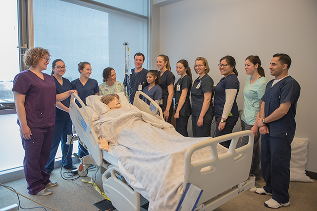 nursing students standing in a semi-circle around a dummy patient in a bed